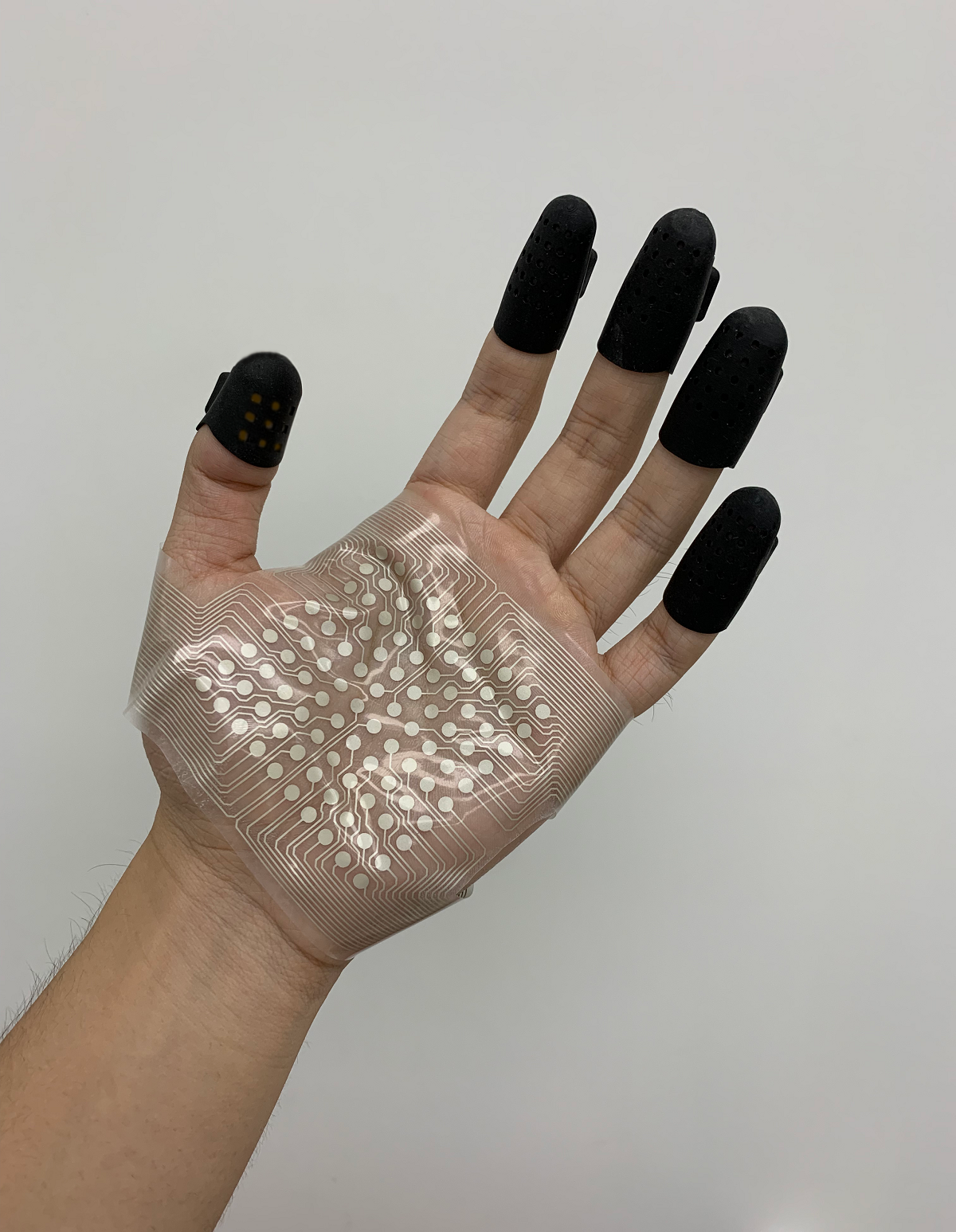 A hand with a grid of electrodes on the palm and black caps on the fingertips