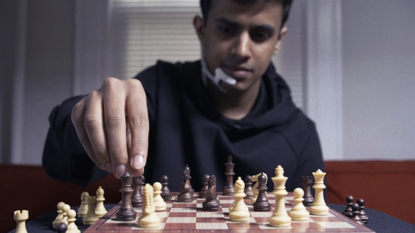 Man wearing a white device on his face that similars the microphone of a headset, playing chess.