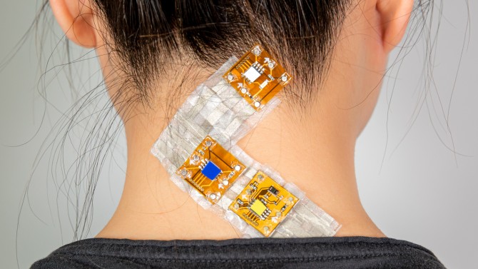 Back of woman's neck with 3 squares of bandaid like material with visible microchips in them on her neck.